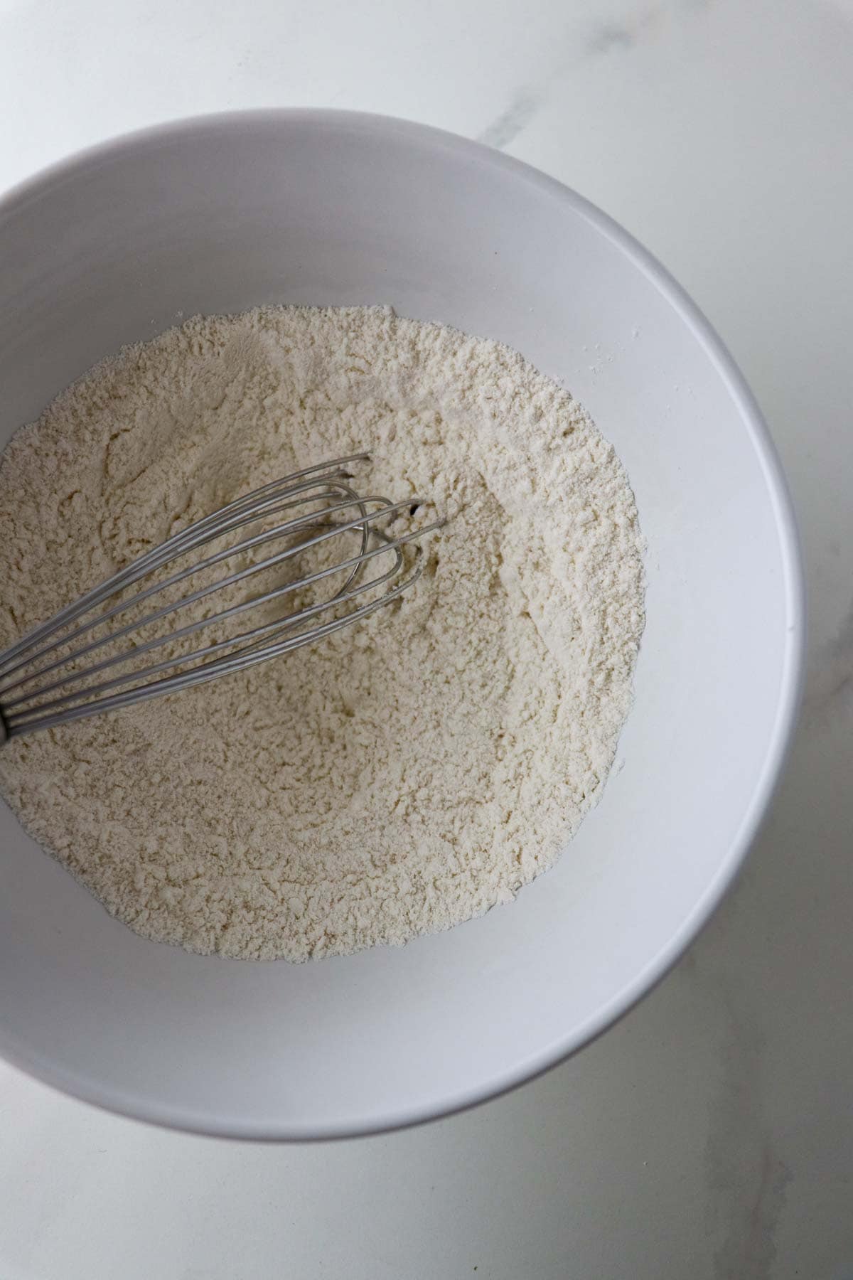 Flour in a white bowl with a whisk.