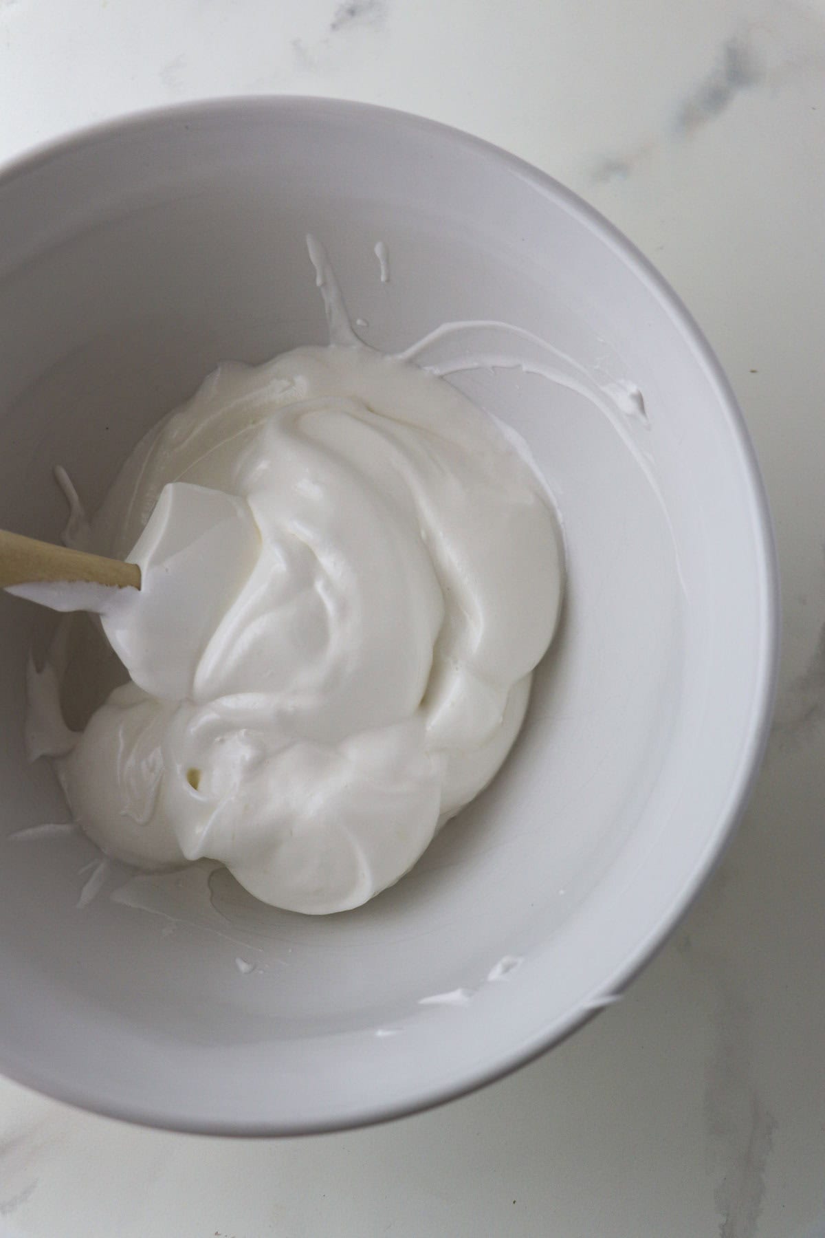Whipped egg whites in a white bowl with a whisk.