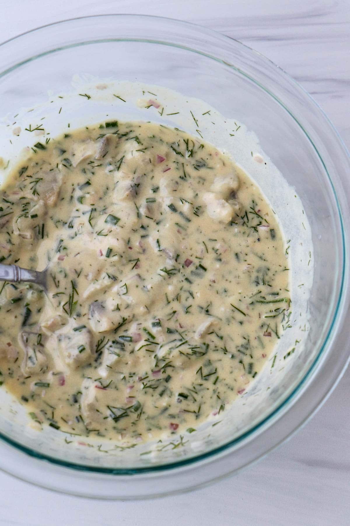 Swedish Mustard Herring in a glass bowl with a spoon.