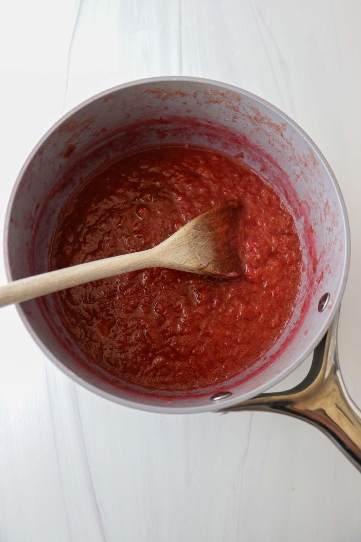 Cooked rhubarb filling for Icelandic Happy Marriage Cake in a saucepan with a wooden spoon.