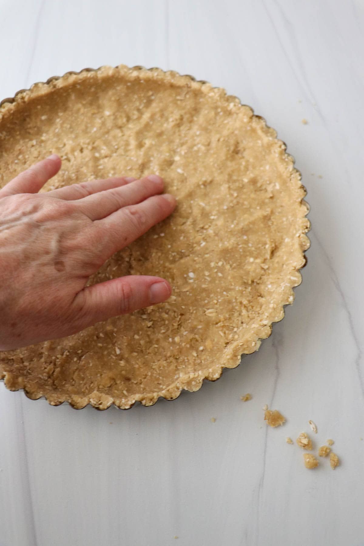 Person patting an oat crust into a tart pan.