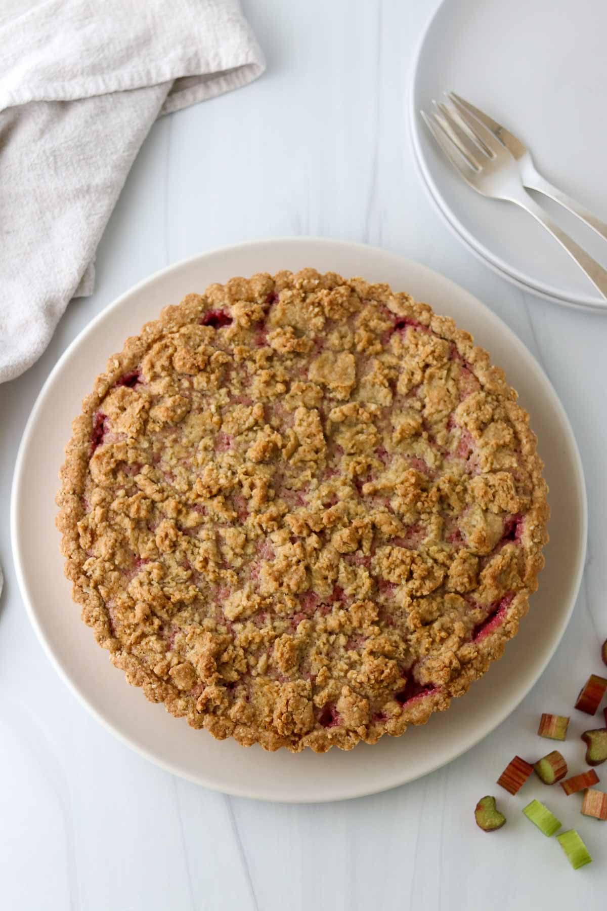 Icelandic Happy Marriage Cake (Hjónabandssaela) on a plate next to forks and serving plates, fresh rhubarb and a napkin.