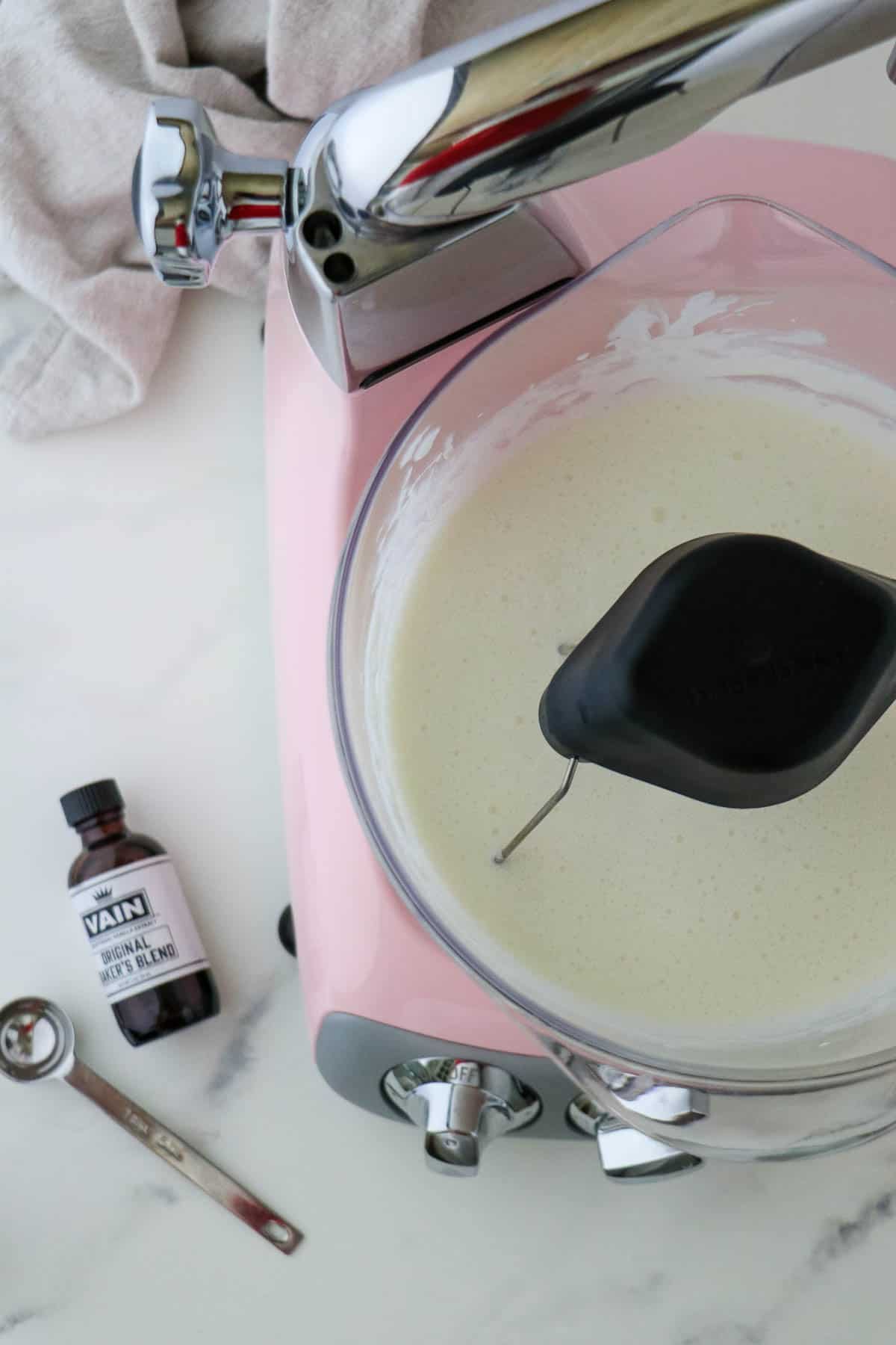 Pink stand mixer next to vanilla extract and a teaspoon.