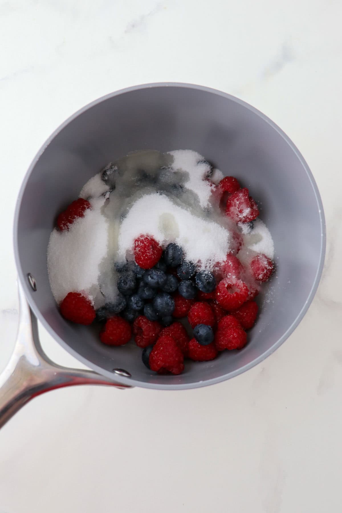 Blueberries and raspberries in a saucepan with sugar.