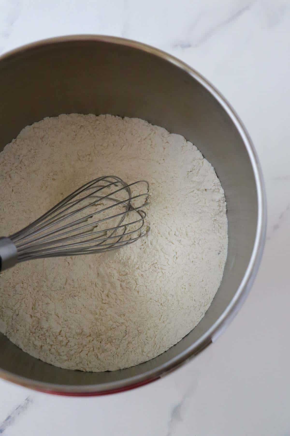 Dry ingredients in metal bowl with a whisk.