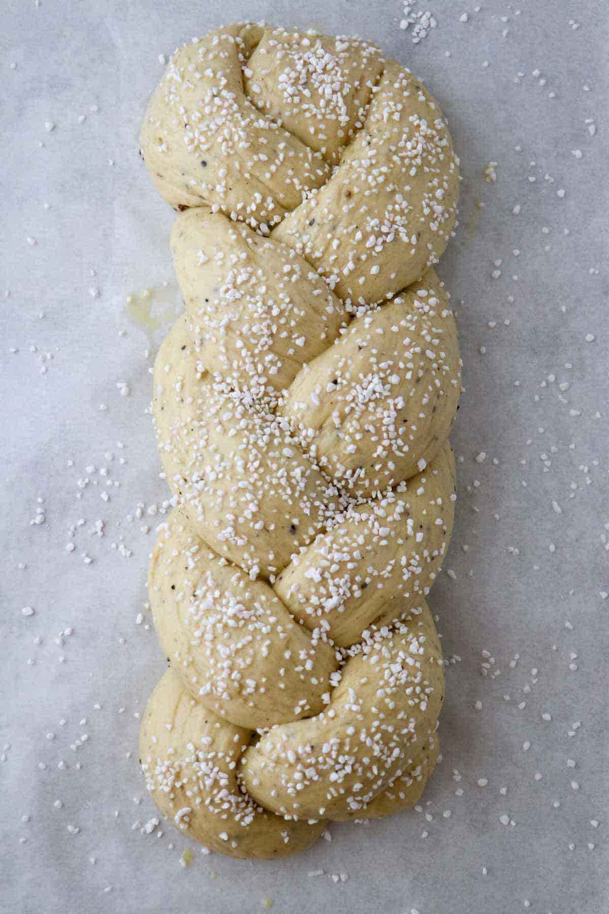 Braided, unbaked loaf of Finnish Cardamom Bread topped with pearl sugar.