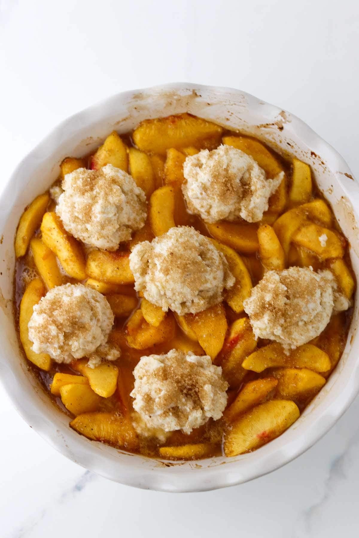 Unbaked Cardamom Peach Cobbler in a white pie plate.