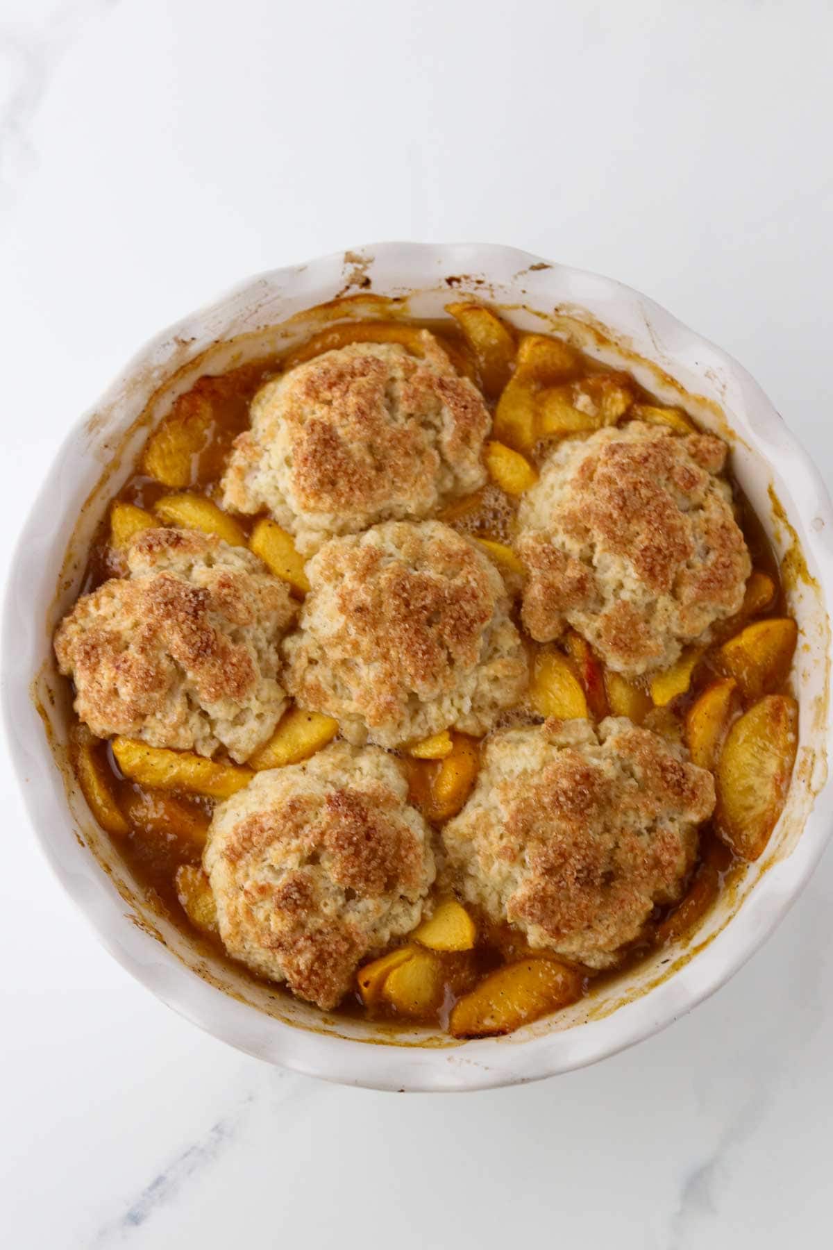 Baked Cardamom Peach Cobbler in a white pie plate.