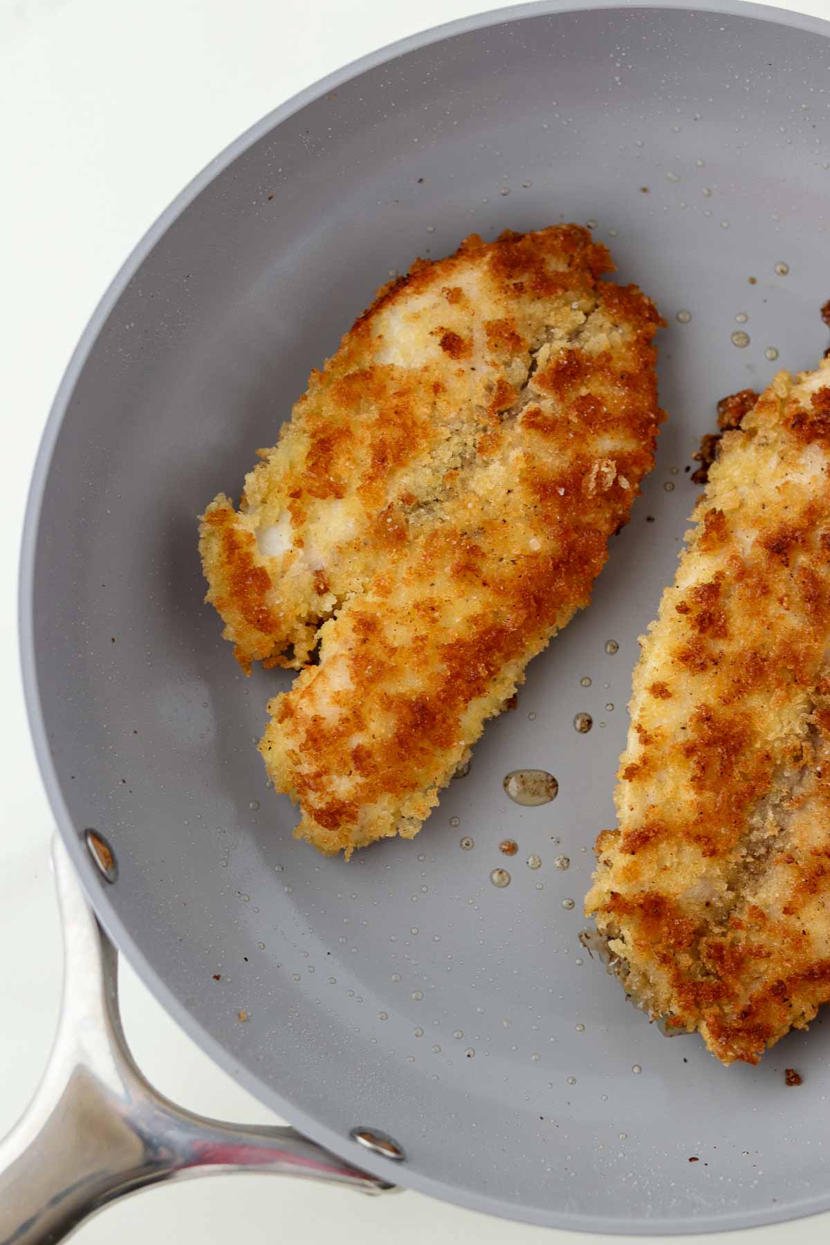 Breaded pan-fried fish in a gray skillet.