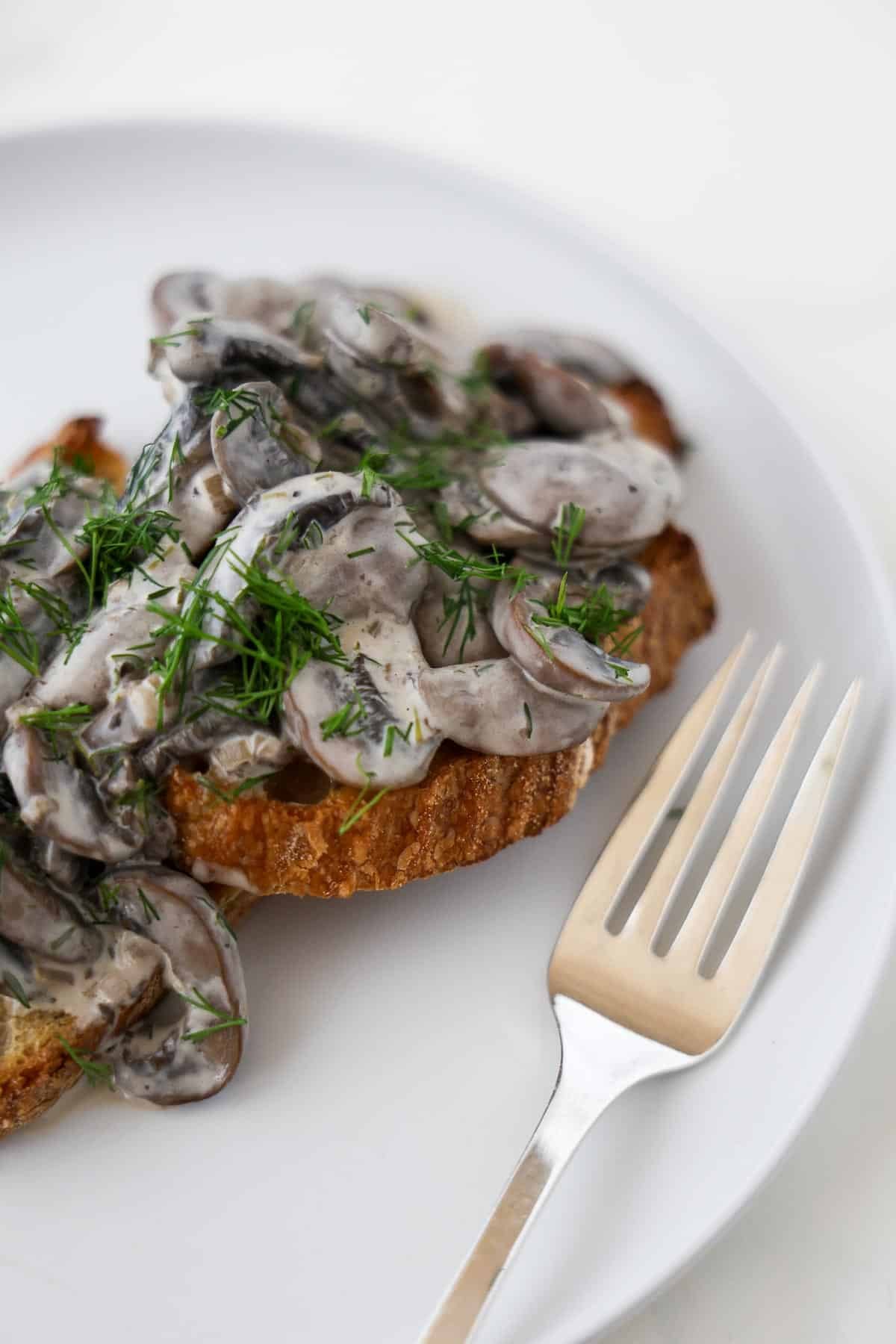 Creamy mushrooms on toast topped with chopped dill next to a fork.