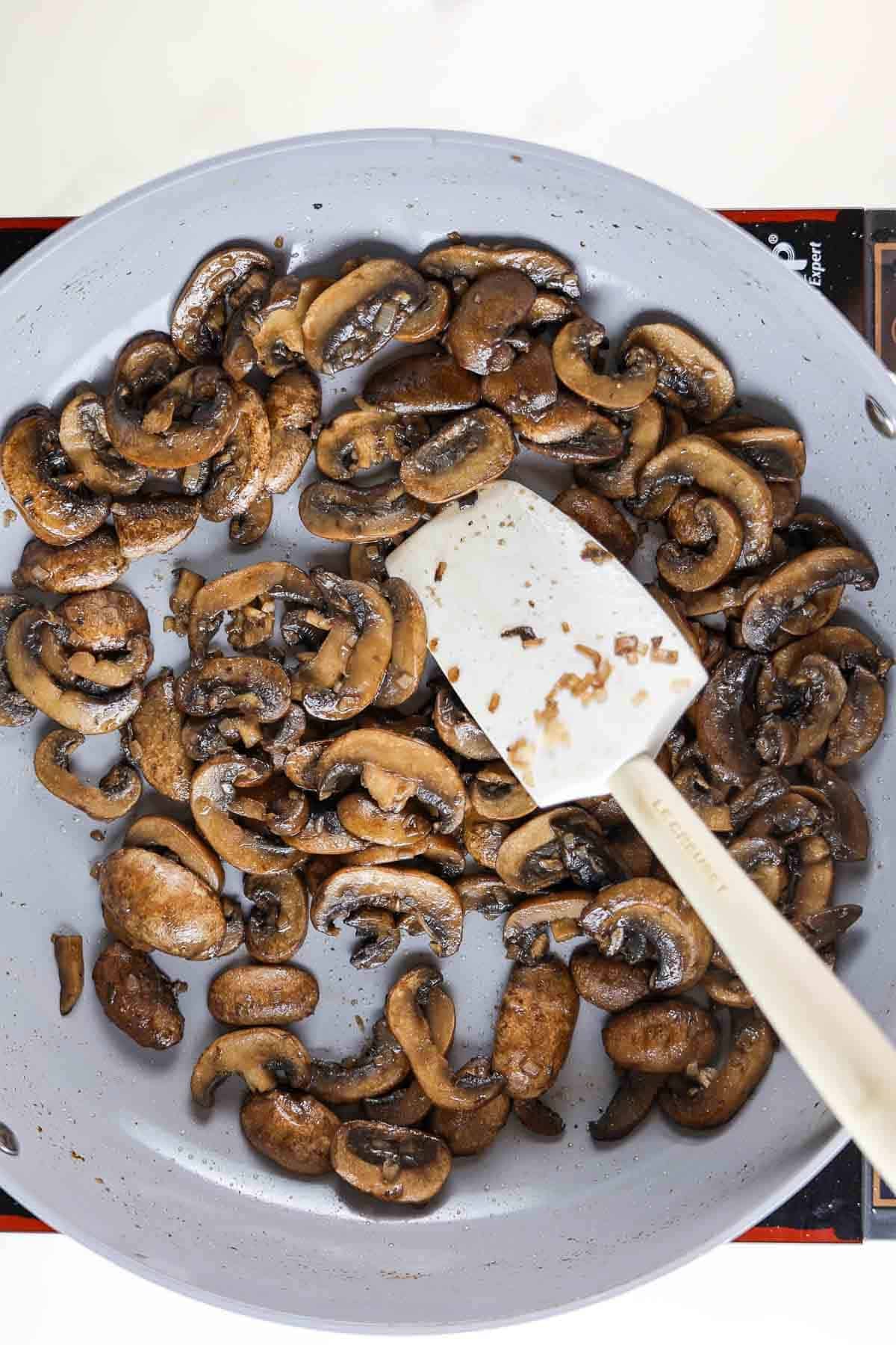 Sauteed mushrooms in a skillet with a rubber spatula.