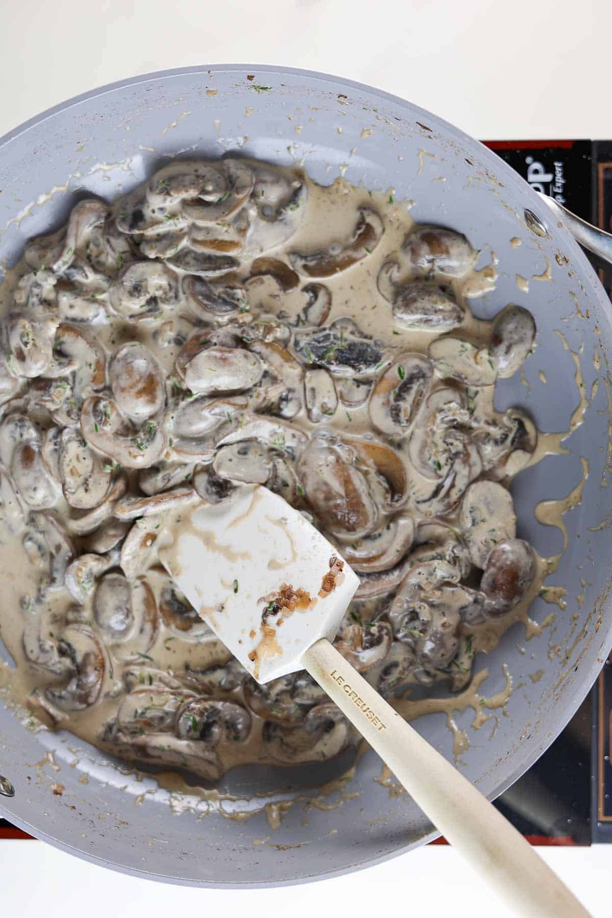 Mushrooms and cream in a skillet with a rubber spatula.