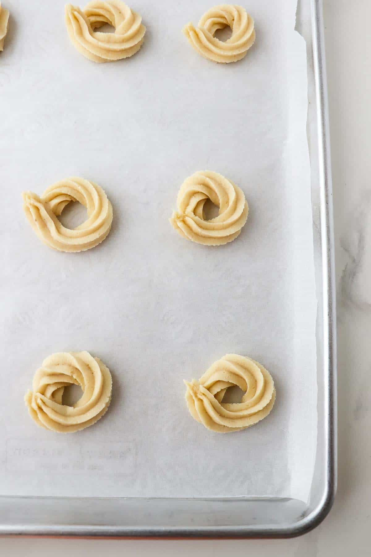 Danish Butter Cookies (Valiljekranse) piped onto a parchment paper-lined baking sheet.