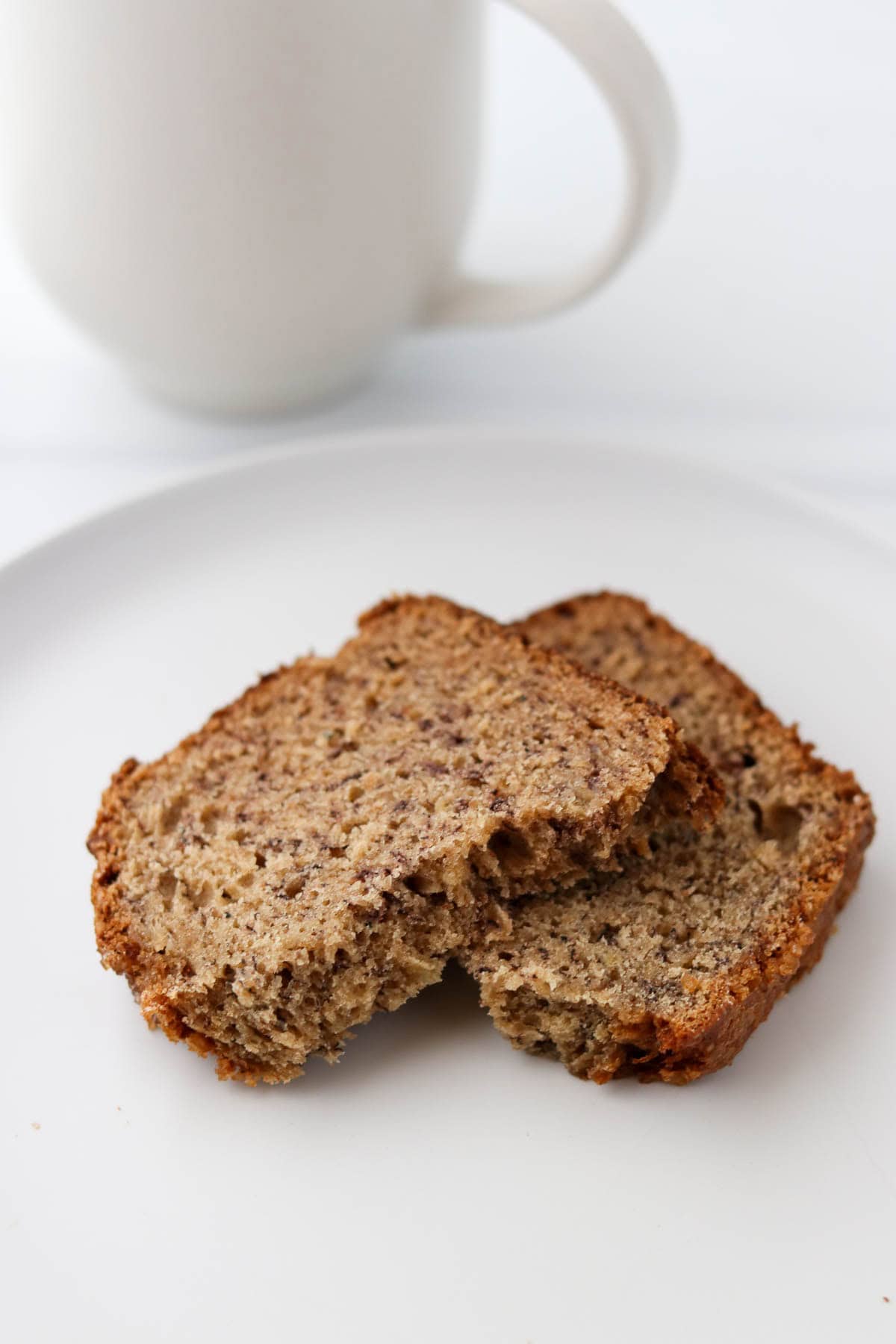 Slice of banana bread broken in two pieces next to a coffee mug.