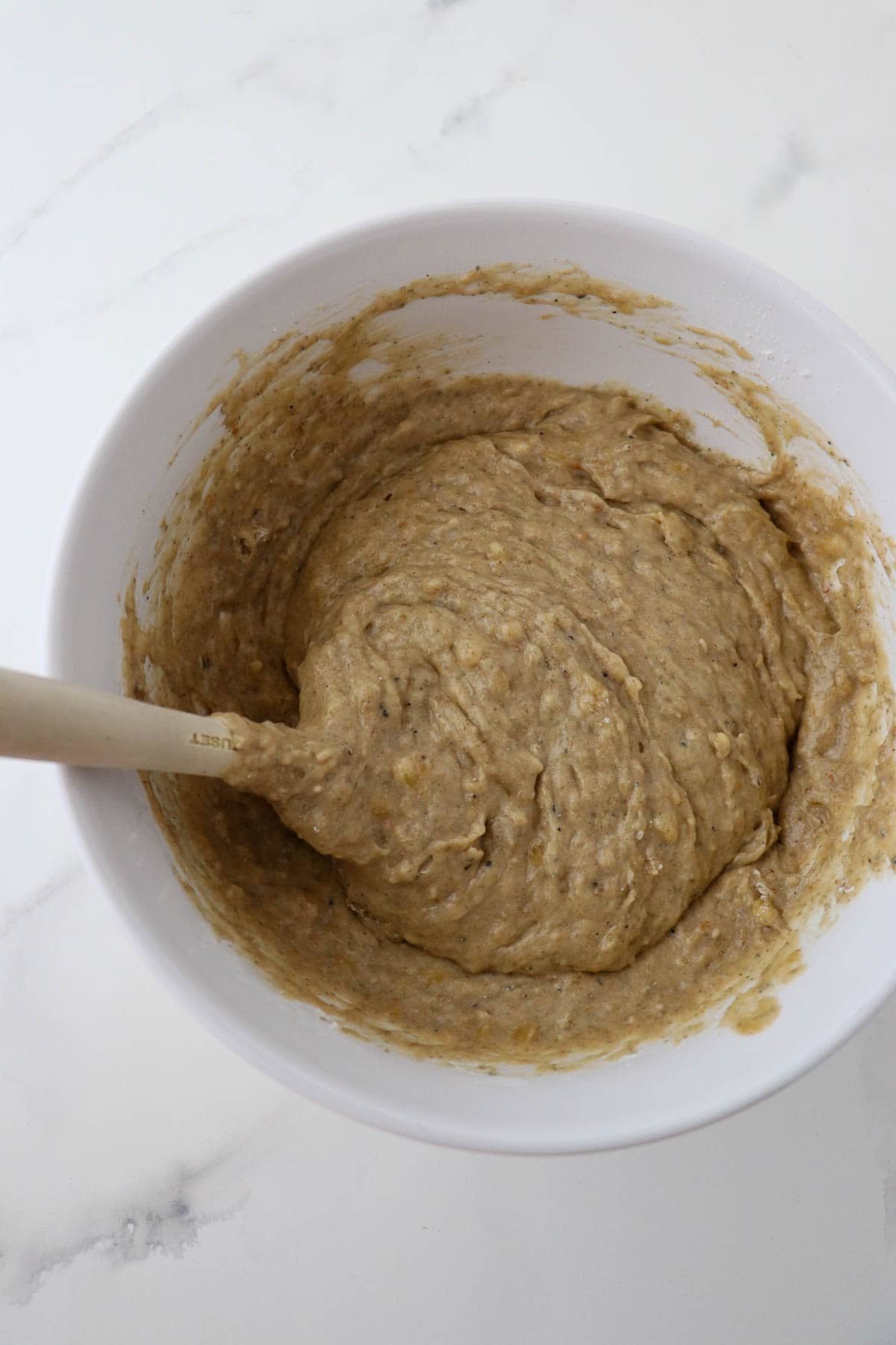 Cardamom Banana Bread batter in a white bowl with a rubber spatula.