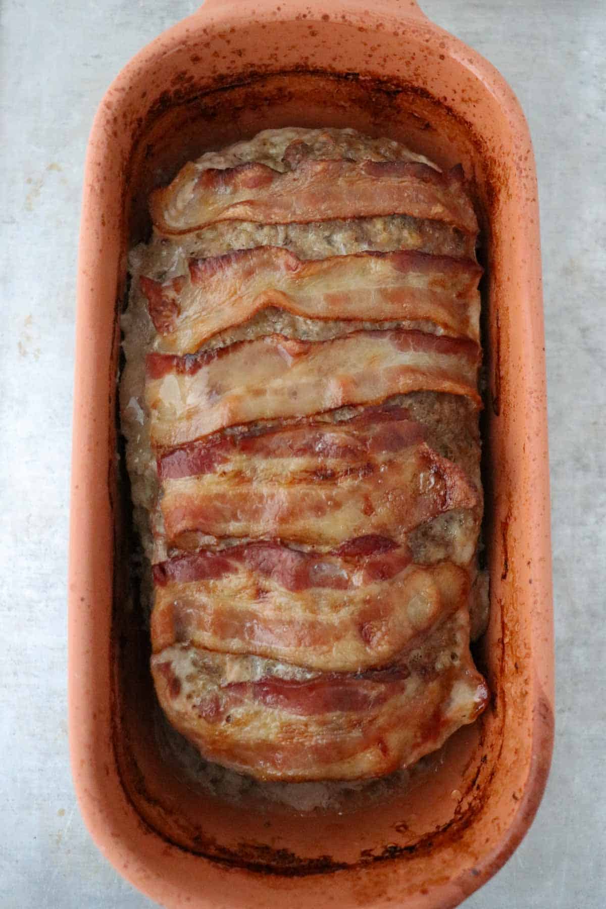 Baked Danish Meatloaf topped with bacon in a clay baker.