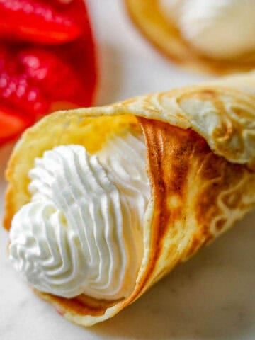 Norwegian Krumkake filled with whipped cream next to cut strawberries.