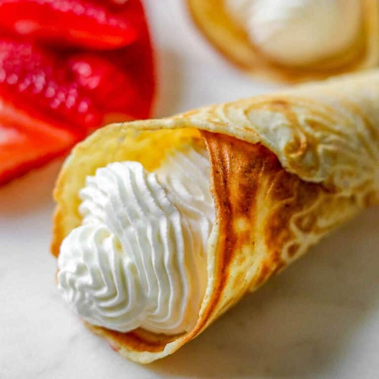 Norwegian Krumkake filled with whipped cream next to cut strawberries.