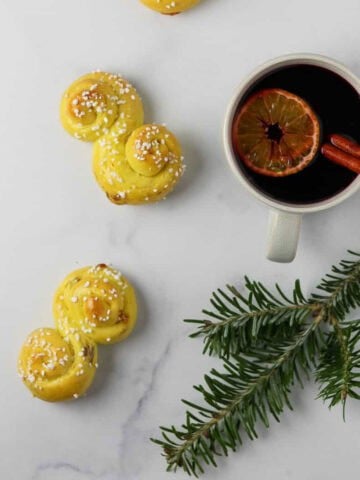 Glögg in a mug next to a St. Lucia Buns and an evergreen branch.