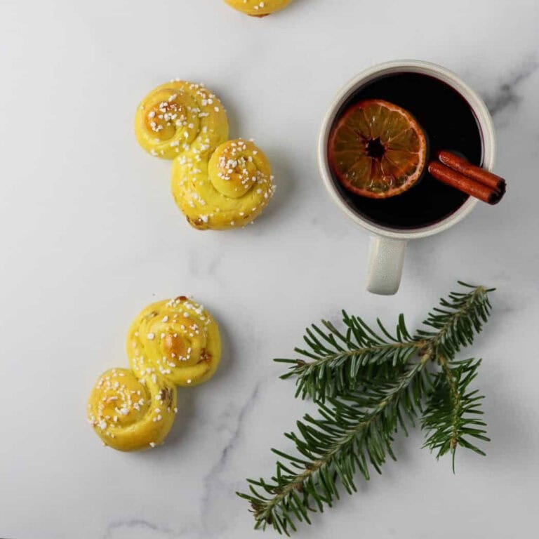 Glögg in a mug next to a St. Lucia Buns and an evergreen branch.