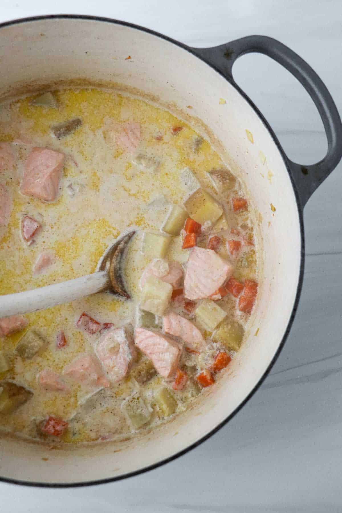 Salmon and vegetables in a creamy broth in a pot with a spoon.