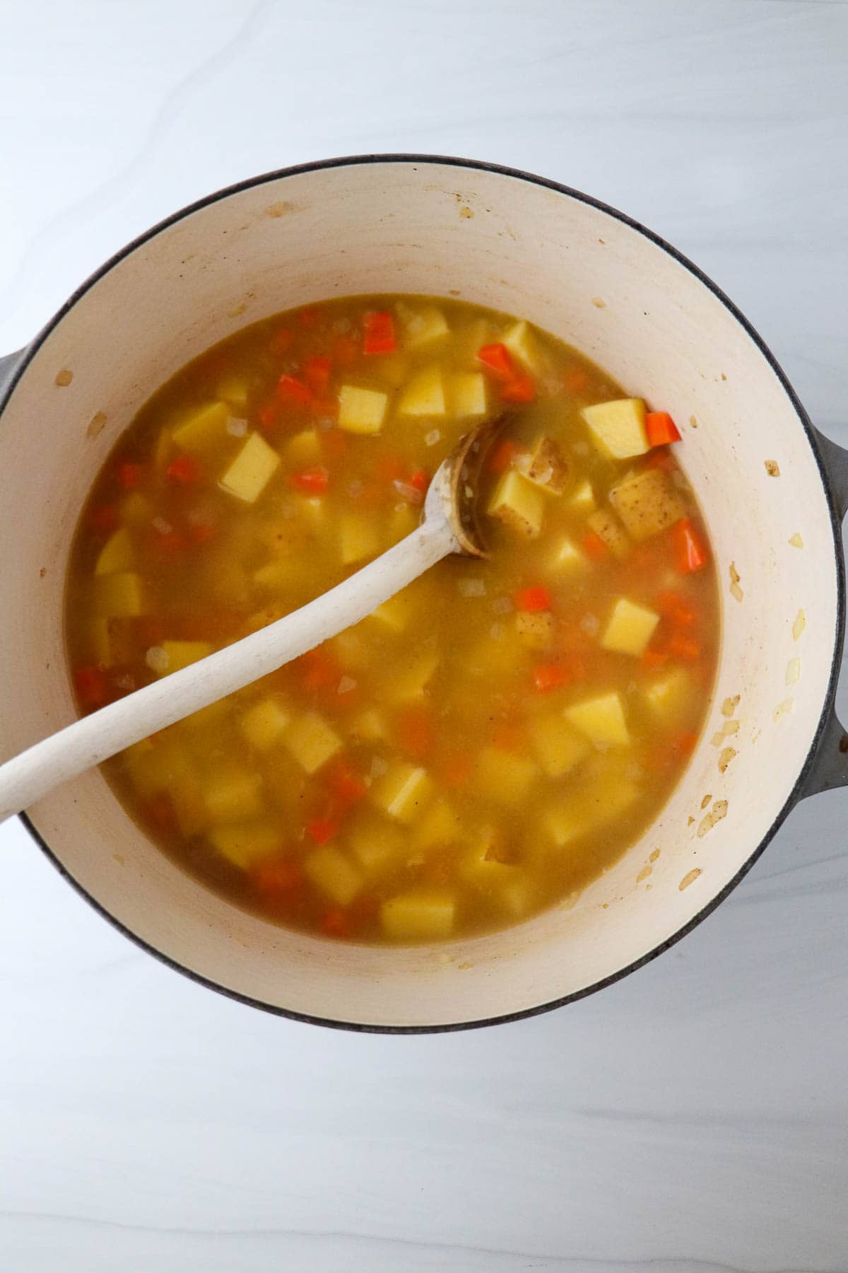 Potatoes, carrots and broth in a pot with a spoon.