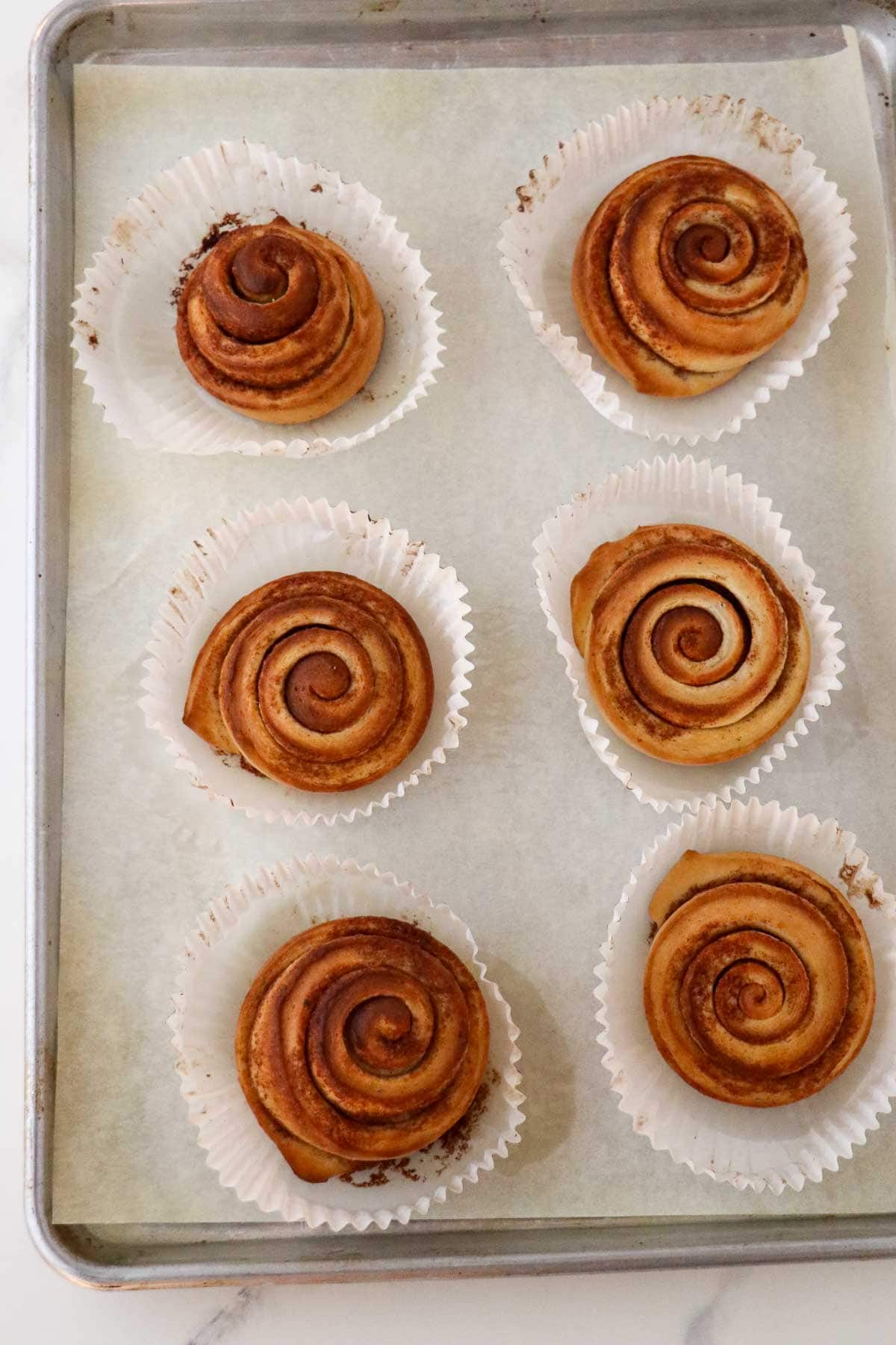 Six baked Norwegian Cinnamon Buns (Skillingsboller) on a baking sheet.