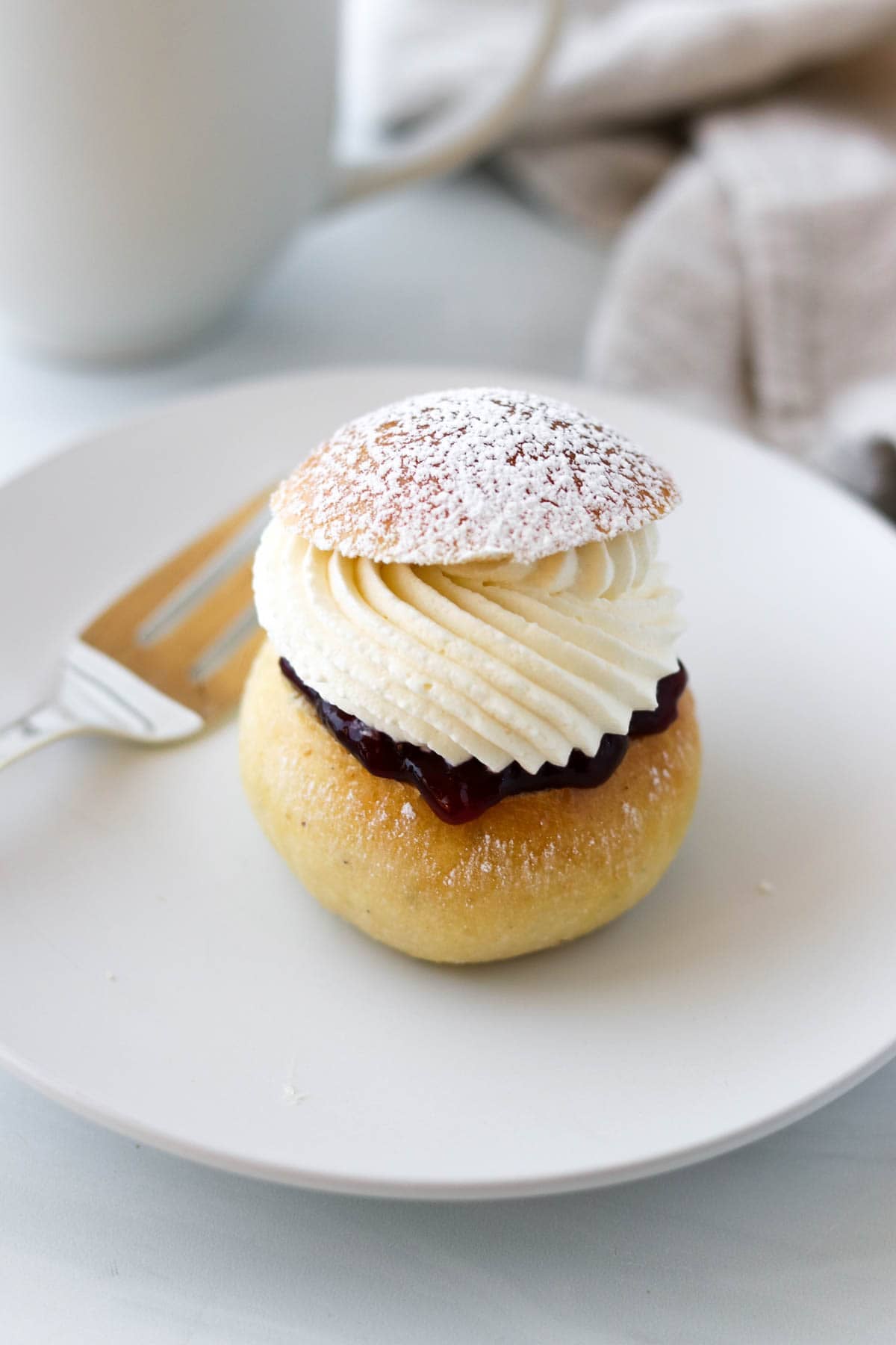 Fastelavnsbolle (Norwegian Lenten Bun) on a white plate next to a fork.