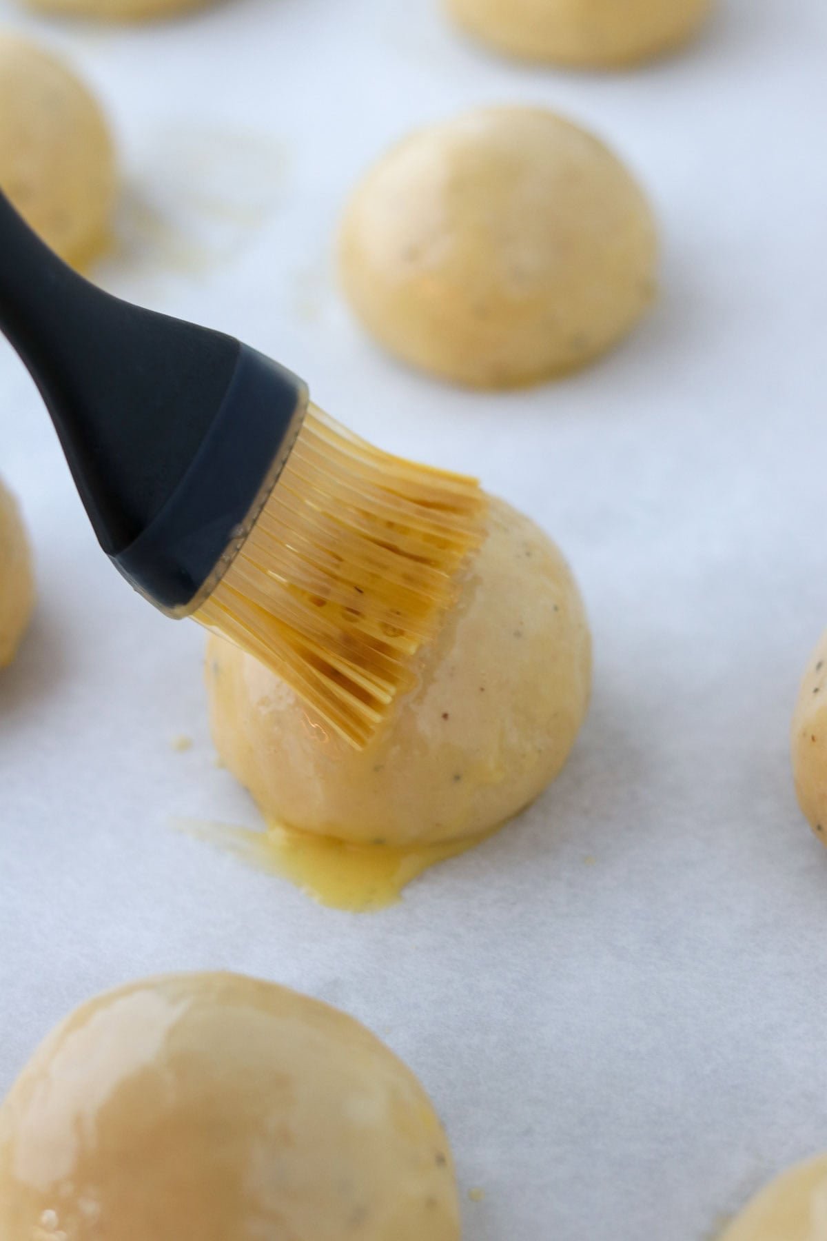 Person brushing Fastelavnsboller (Norwegian Lenten Buns) with egg wash.