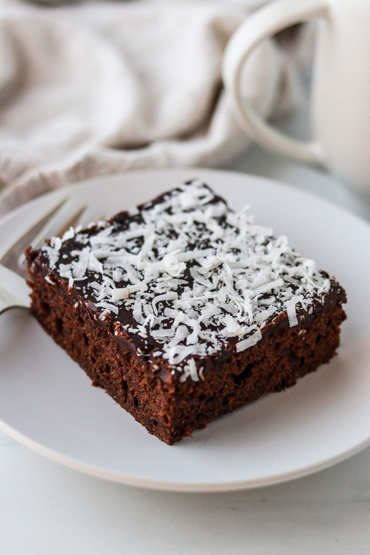 Swedish Love Cake (Kärleksmums) on a white plate next to a fork and coffee mug.