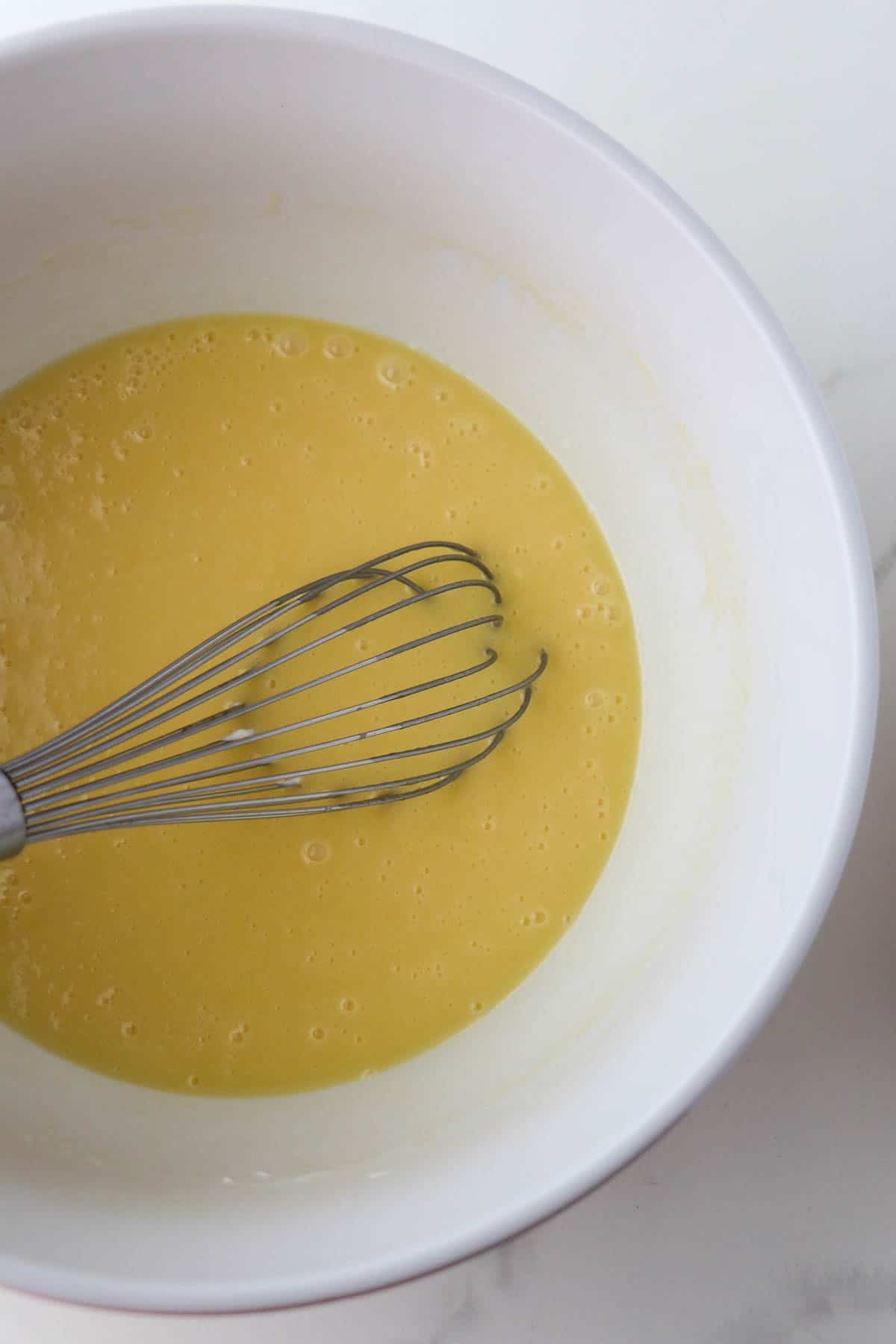 Wet ingredients for Swedish Love Cake (Kärleksmums) in a white bowl with a whisk.