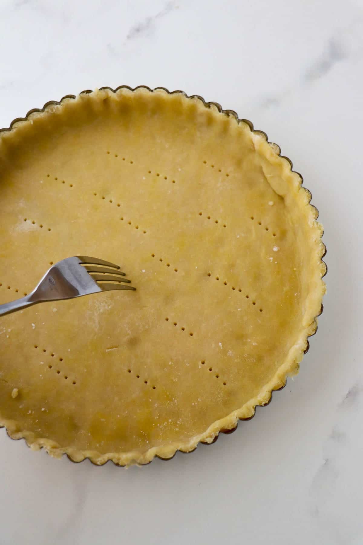 Lingonberry Almond Tart dough in a 9 inch tart pan being pricked with a fork.