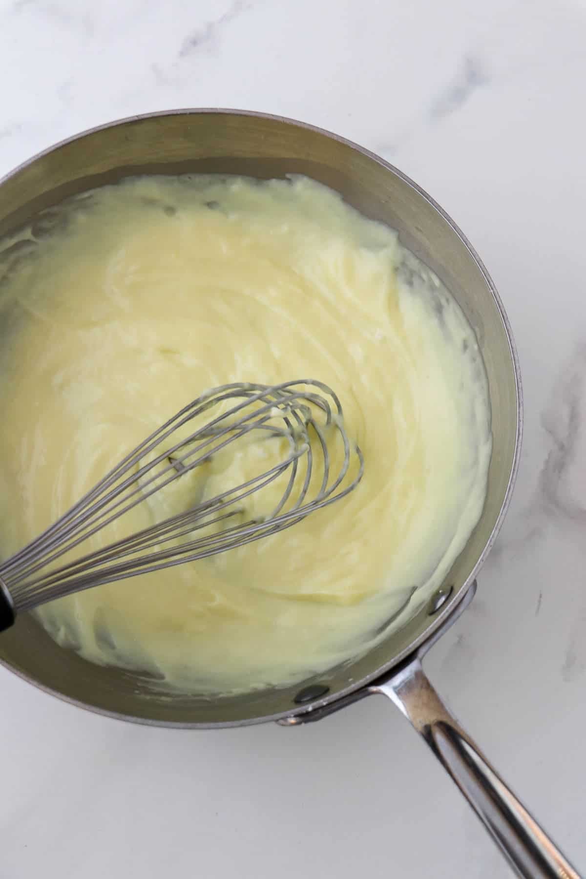 Pastry cream in a saucepan with a metal whisk.