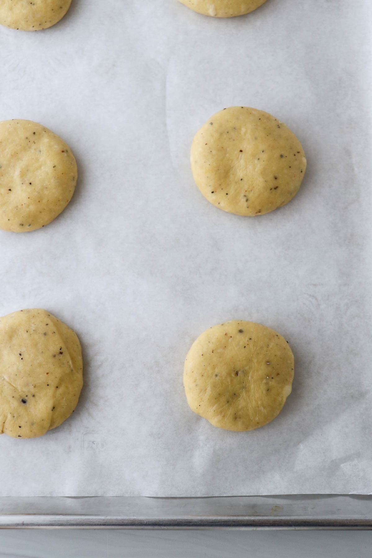 Dough balls that have been flattened into disks on a baking sheet.