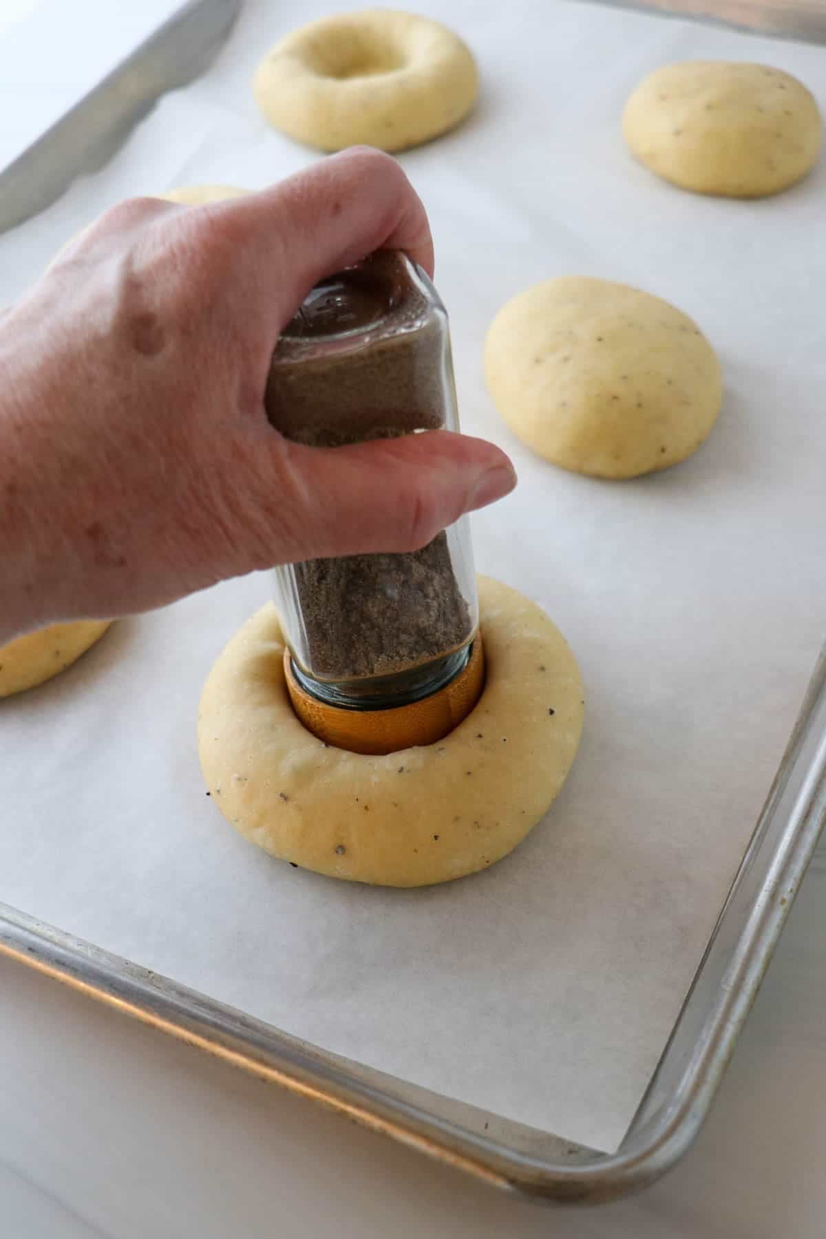 Person pressing a spice jar into a the center of an unbaked bun.