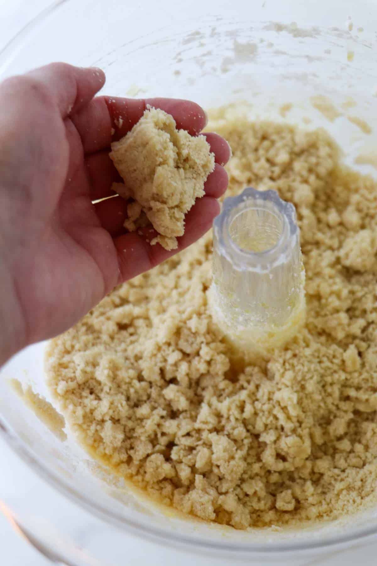 Kolasnittar dough in a bowl with a person squeezing the dough in their hand.