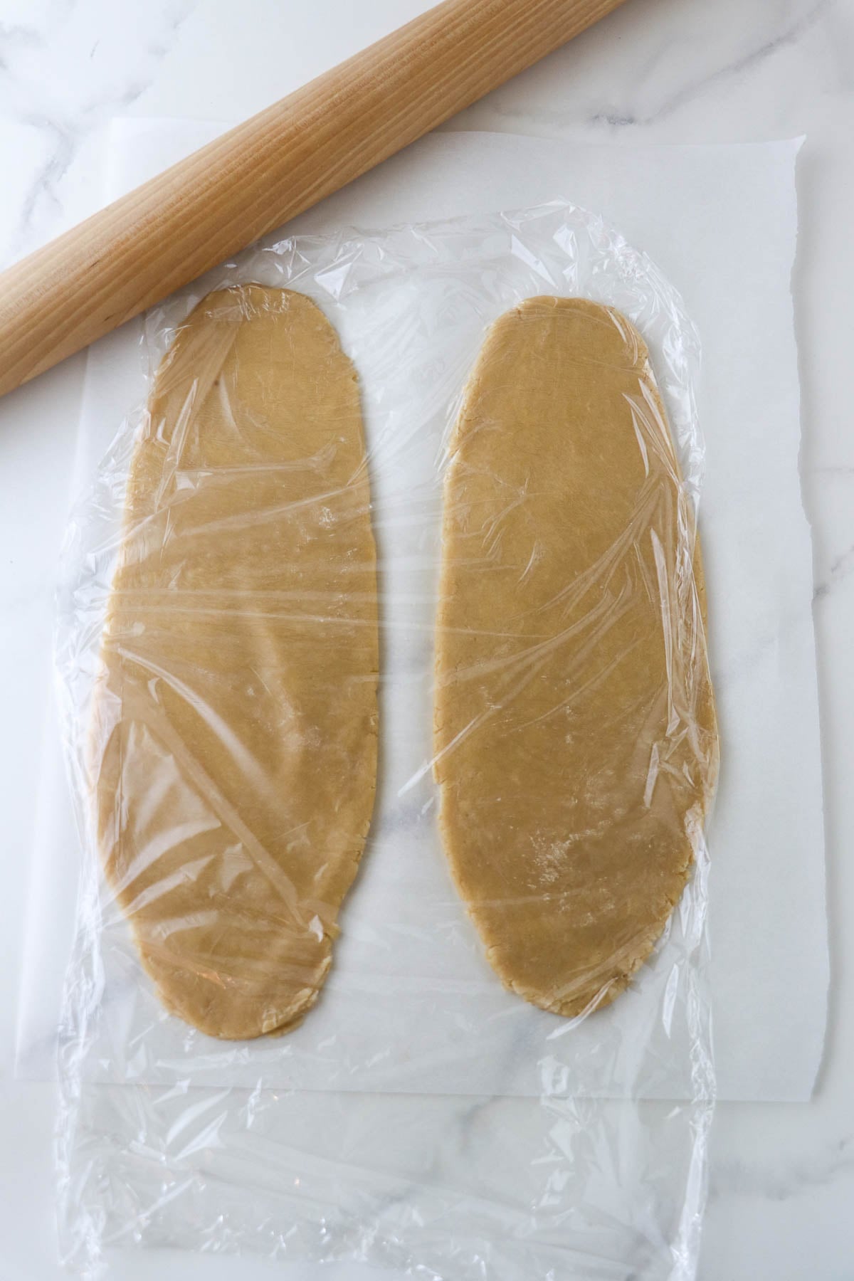 Kolasnittar dough rolled out and covered with plastic wrap and next to a rolling pin.