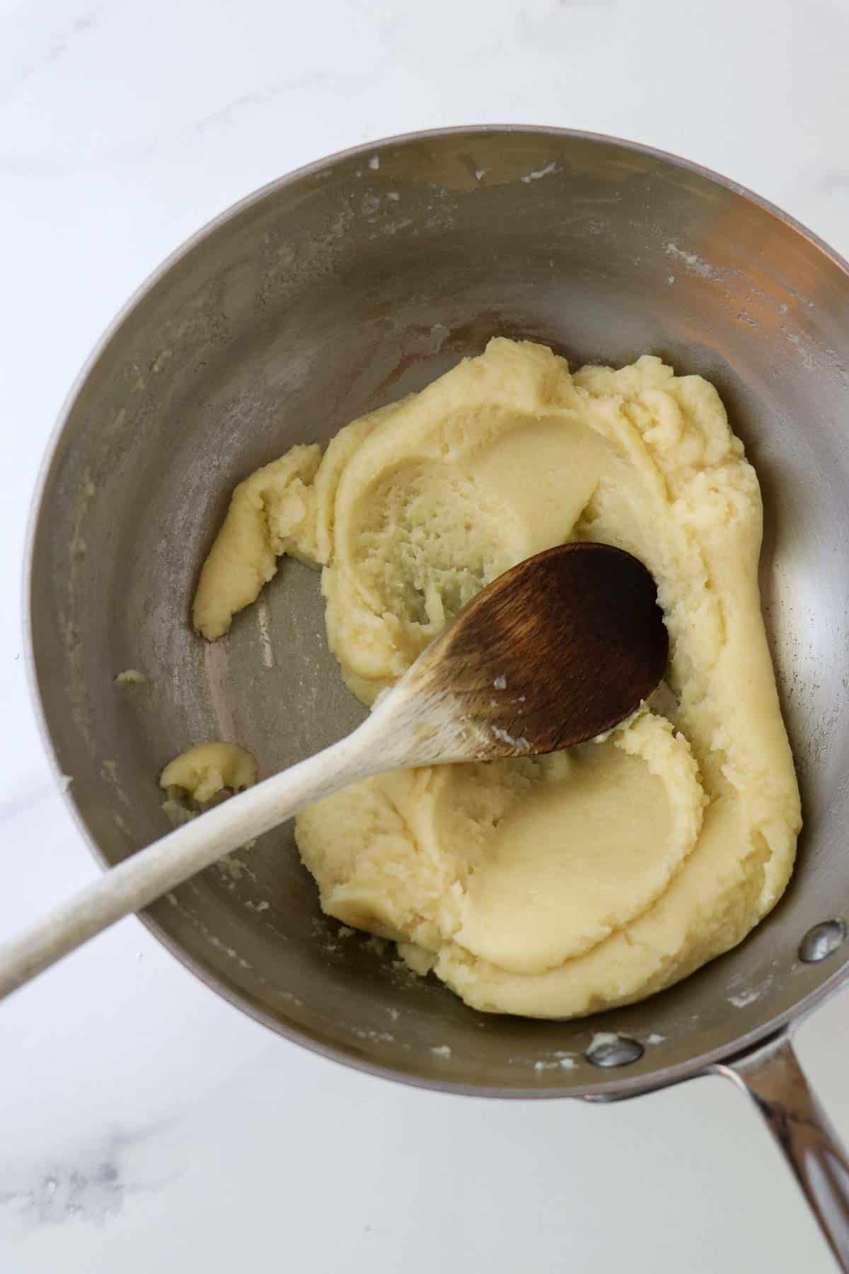 Choux paste in a saucepan with a wooden spoon.