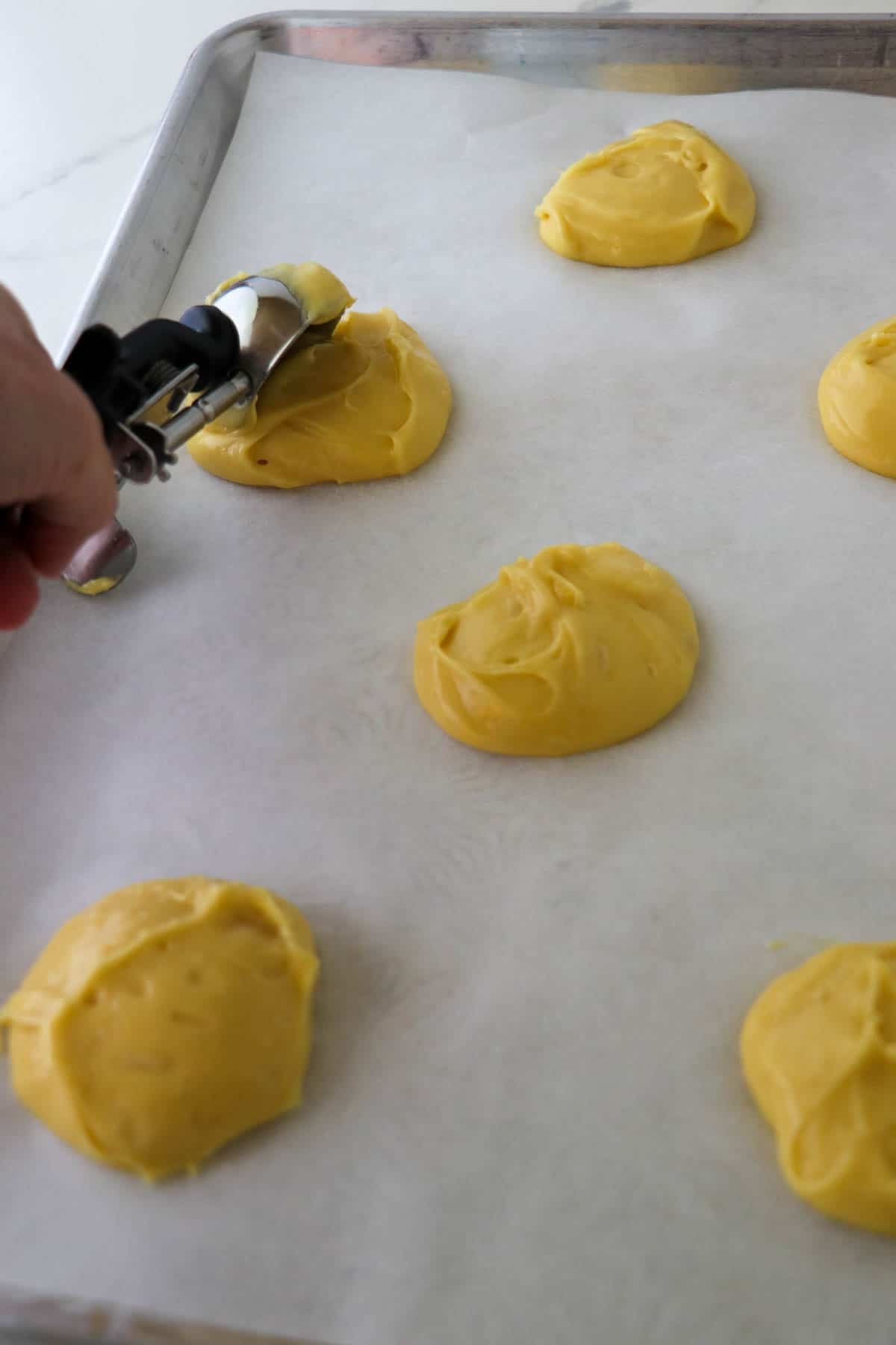 Person spooning choux paste onto a baking sheet.