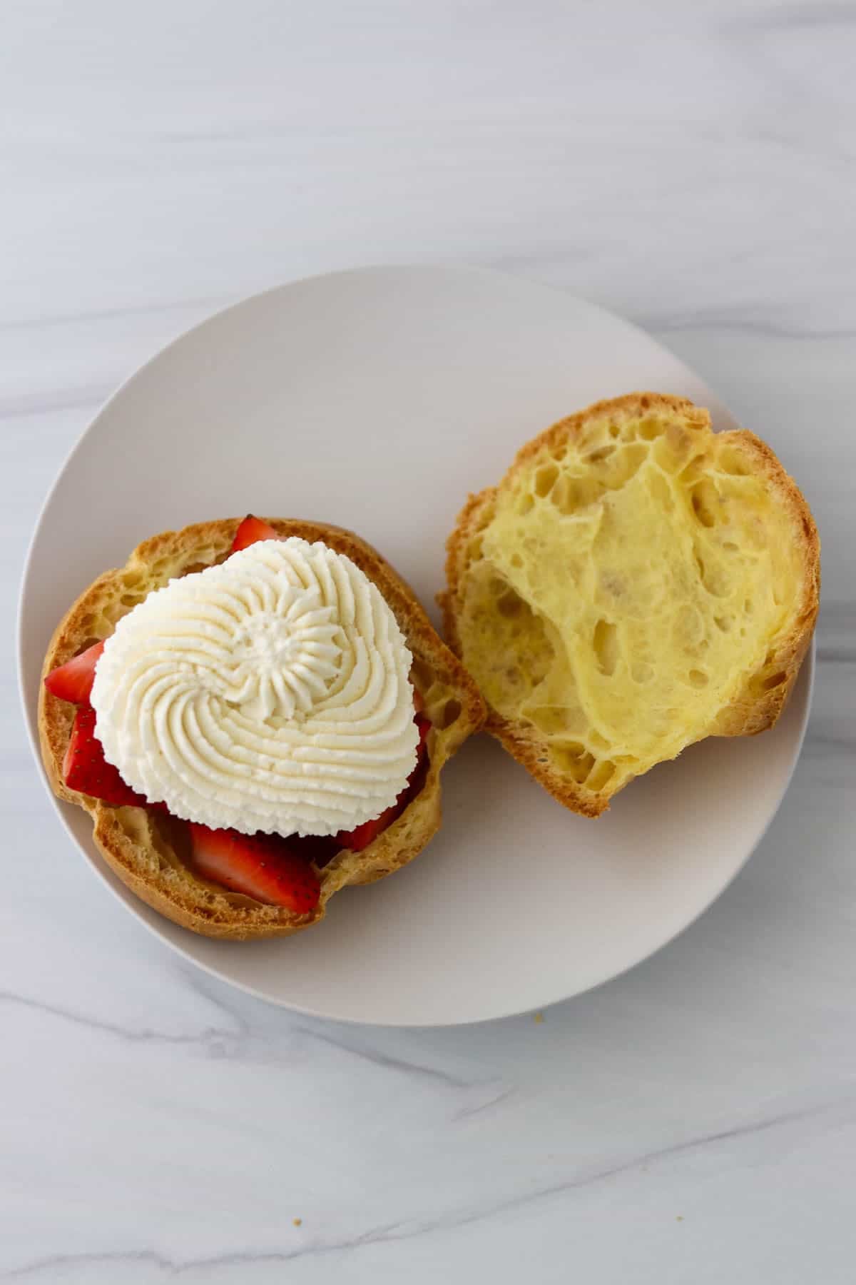 Cream puff topped with strawberries and whipped cream on a white plate.