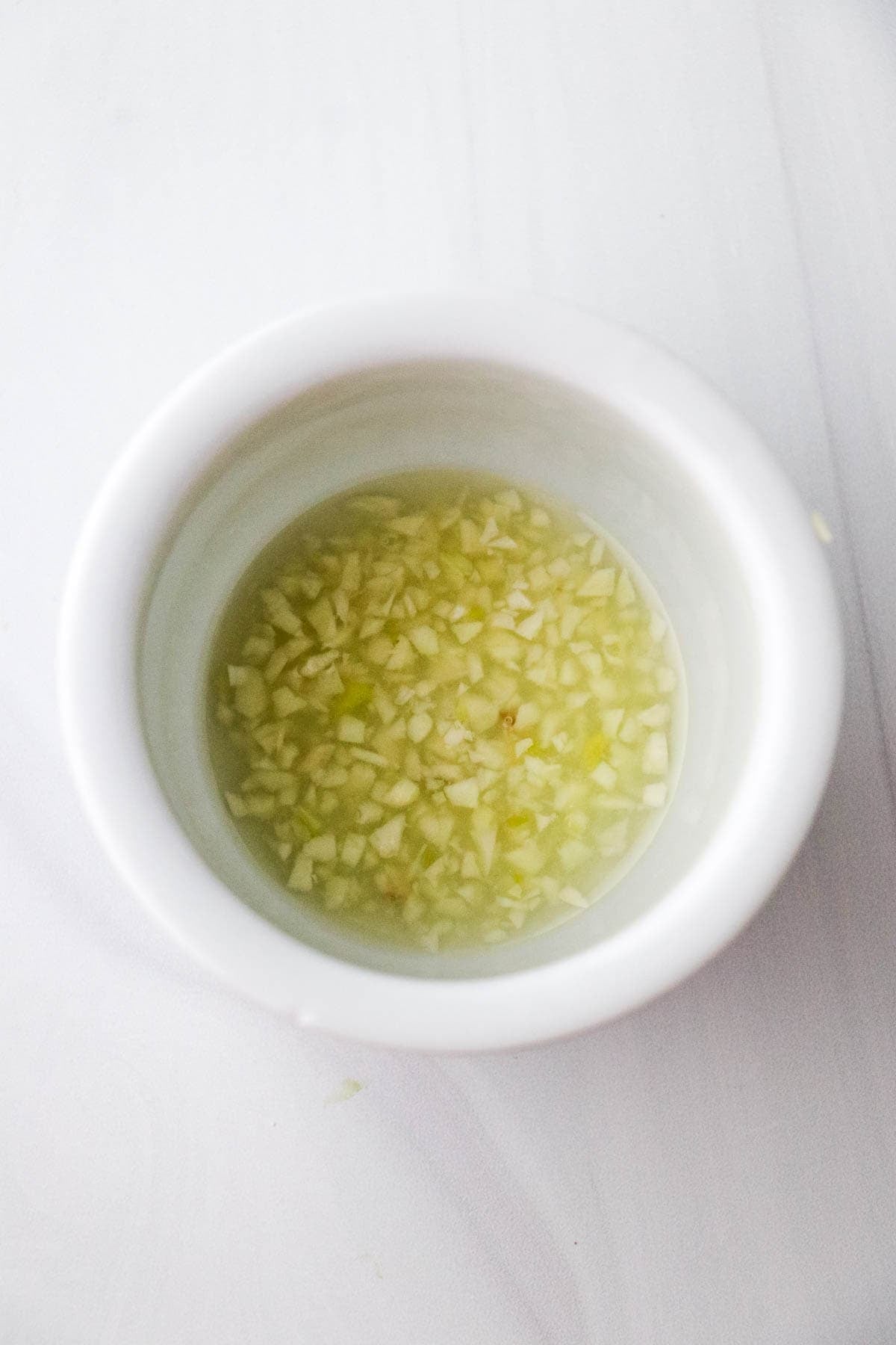 Chopped garlic soaking in lemon juice in a white bowl.