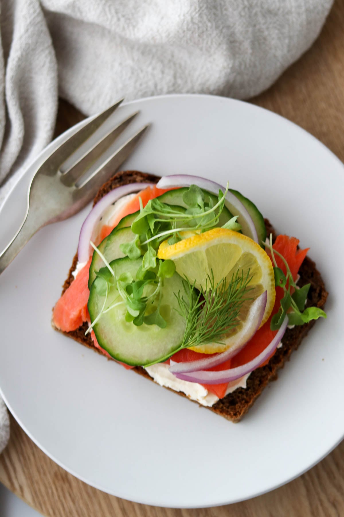 Open-faced smoked salmon sandwich topped with herbed whipped goat cheese, cucumber, pickled onion, lemon and dill.