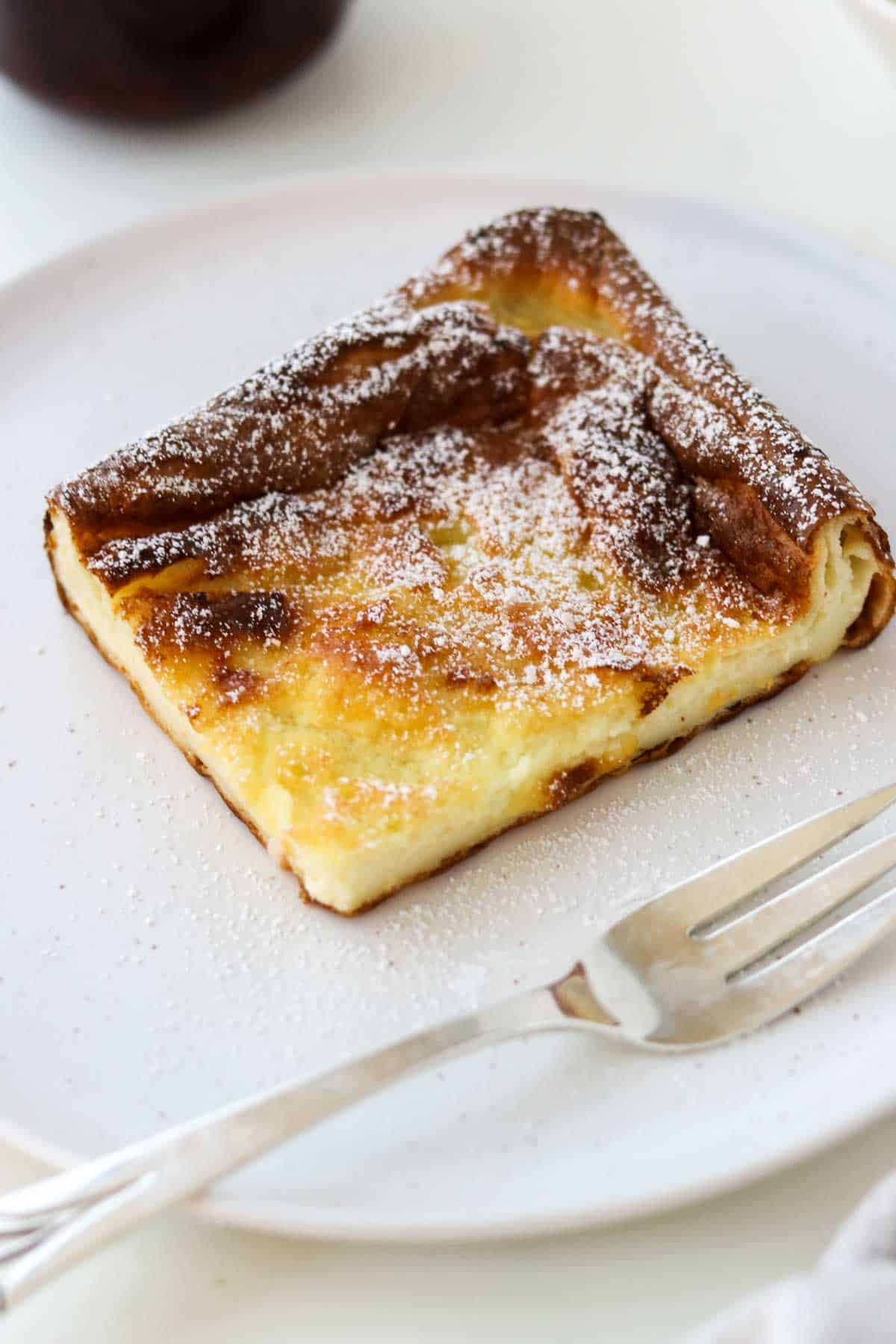 Swedish Oven Pancake (Ugnspannkaka) slice on a white plate next to a fork.