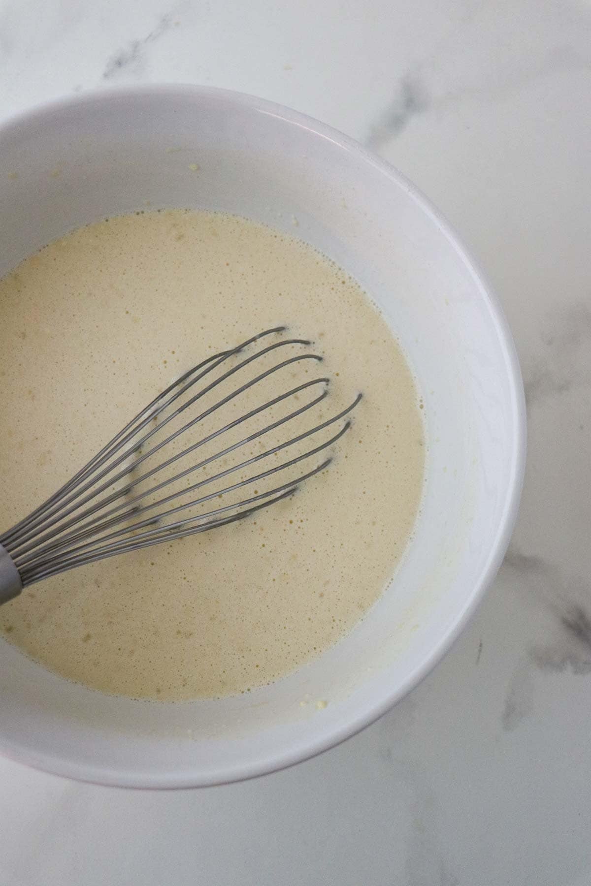 Swedish Oven Pancake (Ugnspannkaka) batter in a white bowl with a whisk.